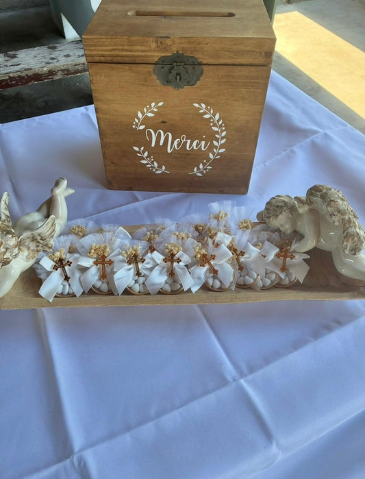 Cadeaux invités Dragées Angels avec rubans blancs et croix dorées devant une urne en bois Merci pour le baptême d'Enzo et Angelo