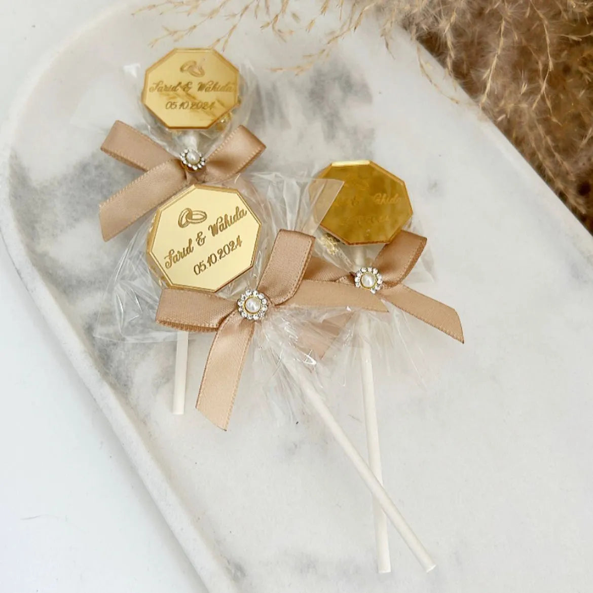 Sucette Glamour personnalisée, décorée d'un ruban élégant et d'un bijou raffiné, idéale comme cadeau pour invités lors de mariages, baptêmes et événements spéciaux.