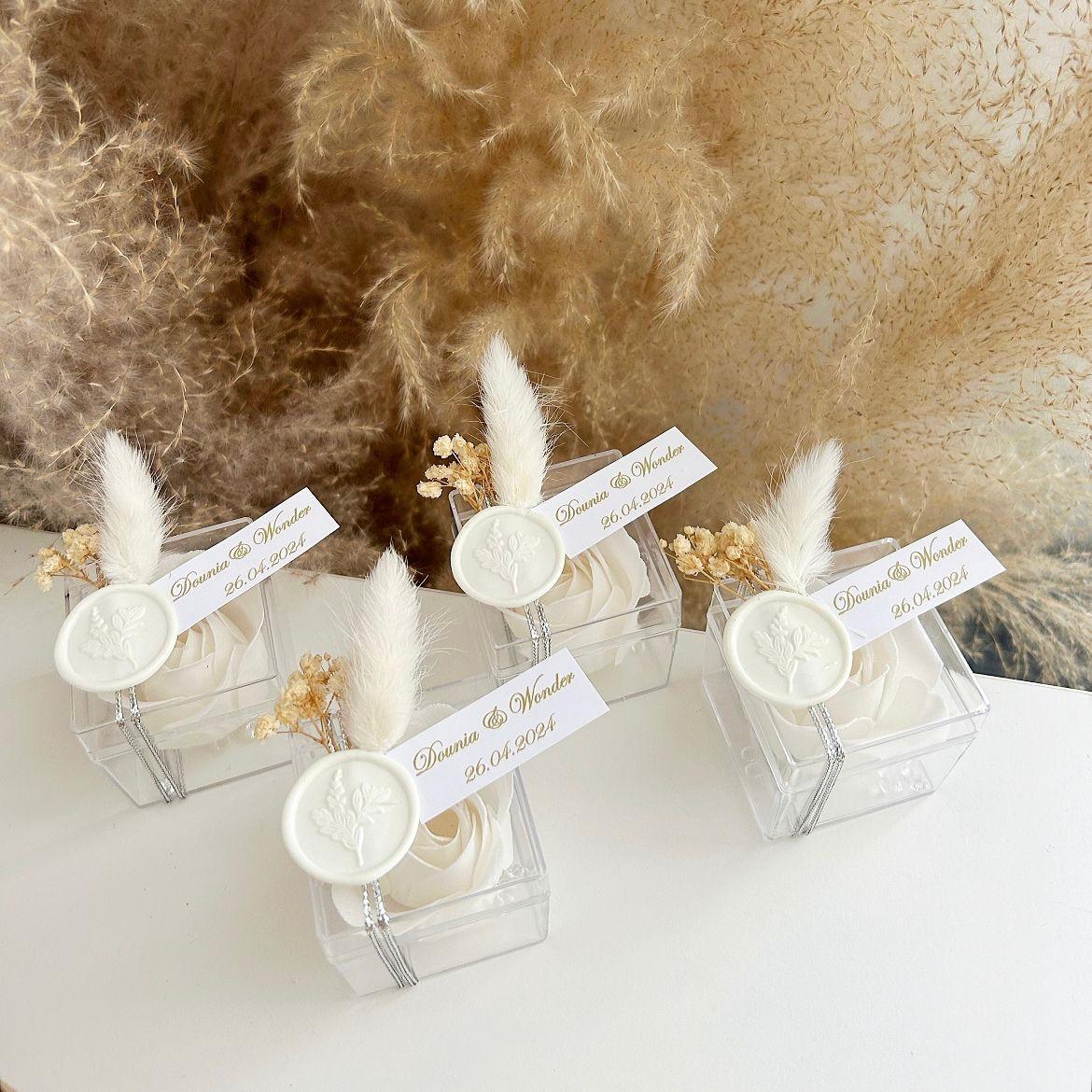 Cadeau invité : rose de savon Sisi en boîte plexi avec plume blanche, sceau décoratif et personnalisation des prénoms.